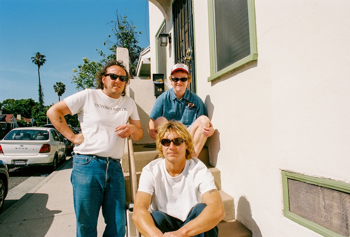 Promotional portrait of Australian pub punk band The Chats posing outdoors on concrete steps in sunny weather.